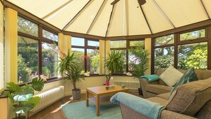 A conservatory with a wooden table, a sofa, and potted plants. - Spernenwyn (St Ives)