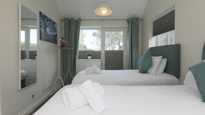 A hotel room with two beds, a large mirror, a painting, and a view of the outdoors. - Spernenwyn (St Ives)