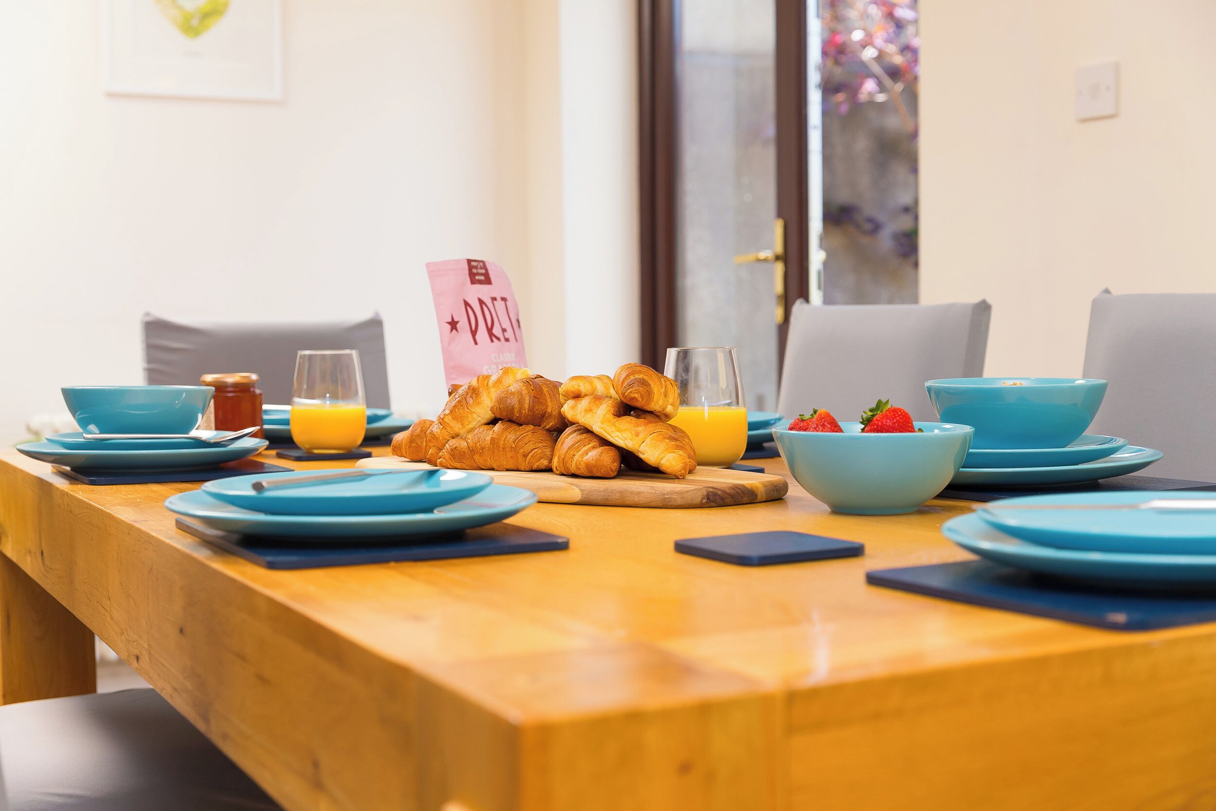 A breakfast table set with croissants, orange juice, and strawberries, with a pink sign reading "PRET".