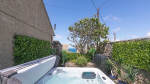A hot tub in a backyard with a stone wall, potted plants, and a view of the ocean. - Spernenwyn (St Ives)