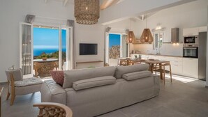 Amplia sala de estar con sofá, mesa de comedor y sillas. Un gran ventanal ofrece vista al mar.