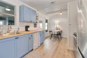 Una cocina con fregadero, armarios, un refrigerador y una zona de comedor con mesa y sillas.