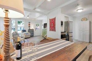 Un coin repas avec une table en bois, des verres à vin et une bouteille. On y trouve également une cuisine avec des placards blancs et un réfrigérateur.