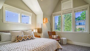 A bedroom with a large bed, two windows, a chair, and a lamp. - Designer 3BR Retreat | Steps from Stadiums (Seattle)