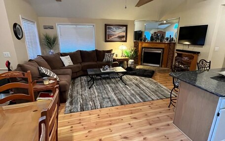 A living room with a sofa, coffee table, and a fireplace. There is a dining table with chairs and a kitchen area with a countertop.