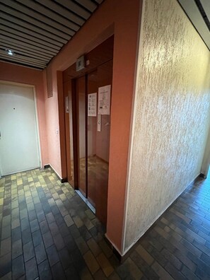 Un couloir doté d’un sol carrelé, d’une porte et d’un mur à surface texturée.