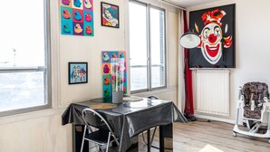 A dining area with a table and chairs, a window with a view, and a large painting on the wall. - GuestReady - Glimpse of dawn in Asnières-sur-Seine (Asnières-sur-Seine)