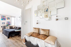 Een moderne slaapkamer met een groot bed, een bureau en een stoel. Er zijn meerdere spiegels aan de muur en een kroonluchter.