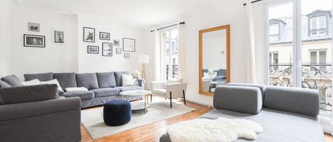 Un salón moderno con sofás grises, un sillón blanco, una mesita redonda y un espejo grande.