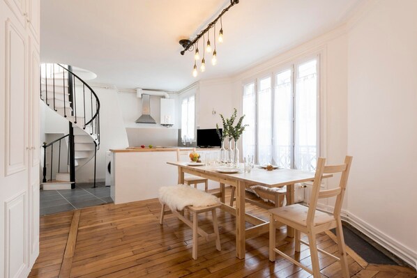 A modern kitchen with a wooden dining table, white chairs, and a staircase leading to another room. - GuestReady - Bright and Spacious Duplex in 5th Arr (Paris)