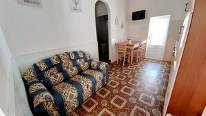 A living room with a patterned sofa, a dining area with a table and chairs, and a TV mounted on the wall. - Three-room apartment with sea view terrace, free private parking, beach at 200mt (Peducelli)