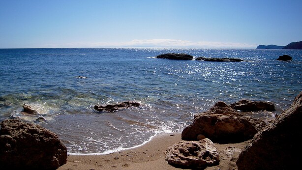 A beach with clear water, rocks, and a distant mountain. - Three-room apartment with sea view terrace, free private parking, beach at 200mt (Peducelli)