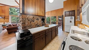 A spacious kitchen with wooden cabinets, a stone fireplace, a large island, and a view of the outdoors. - Starry Skies - West Shore Cabin.  Walk to Private Beach. DOG OK (Tahoe City)