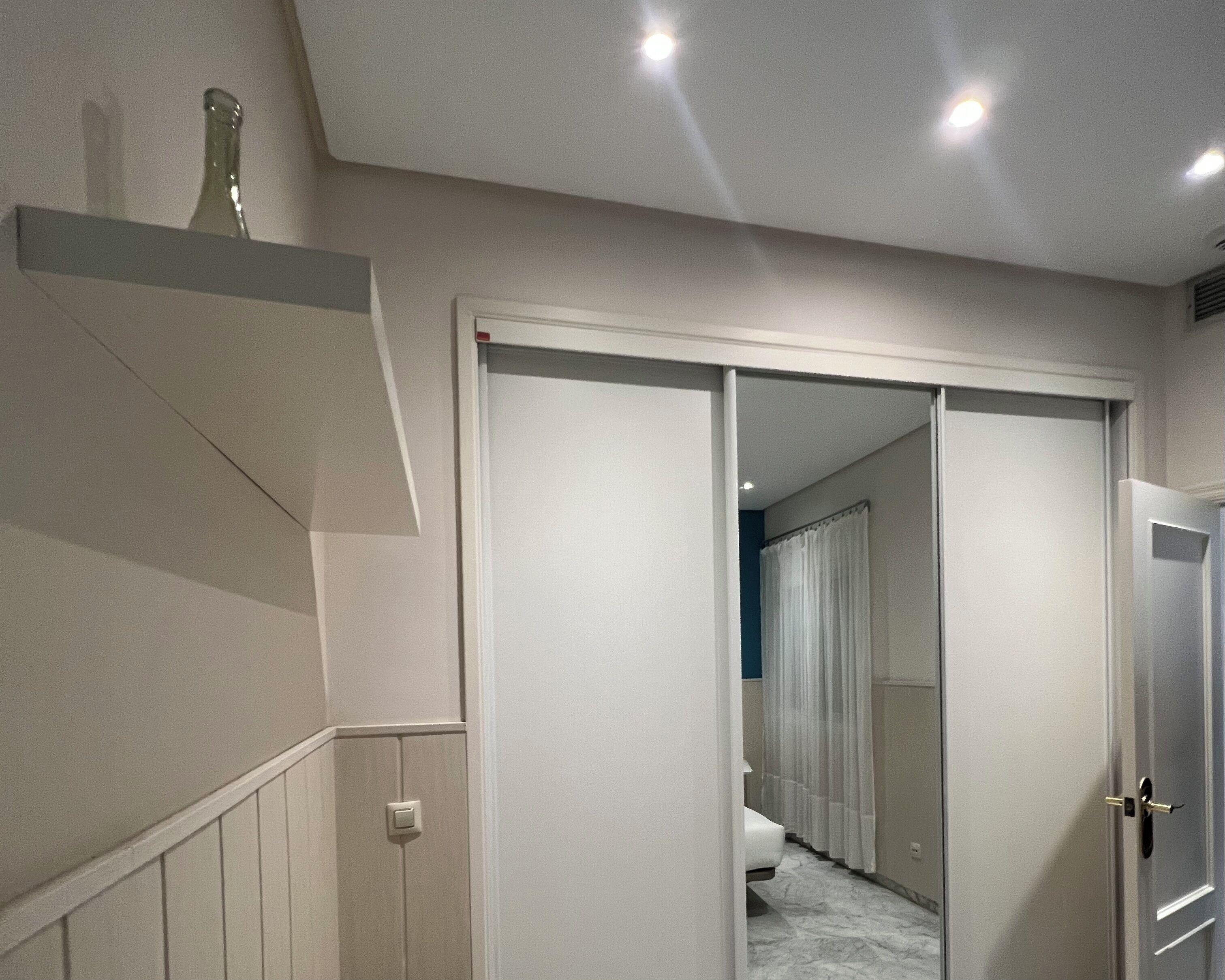 A hallway with a closed door, a light switch, and a small shelf with a bottle.