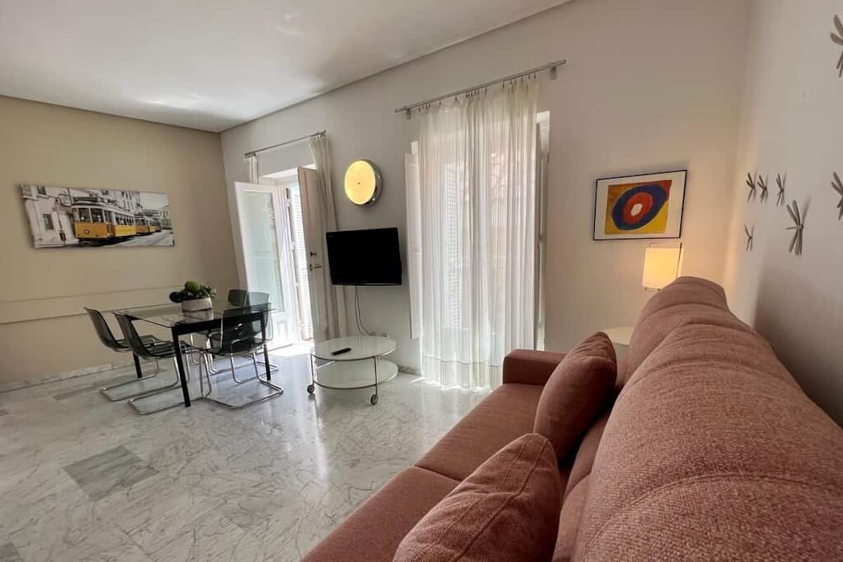 A living room with a sofa, a dining table with chairs, a TV, and a painting on the wall.