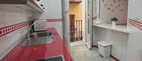 Una cocina estrecha con paredes de azulejos blancos, una encimera roja y un cubo de basura pequeño.