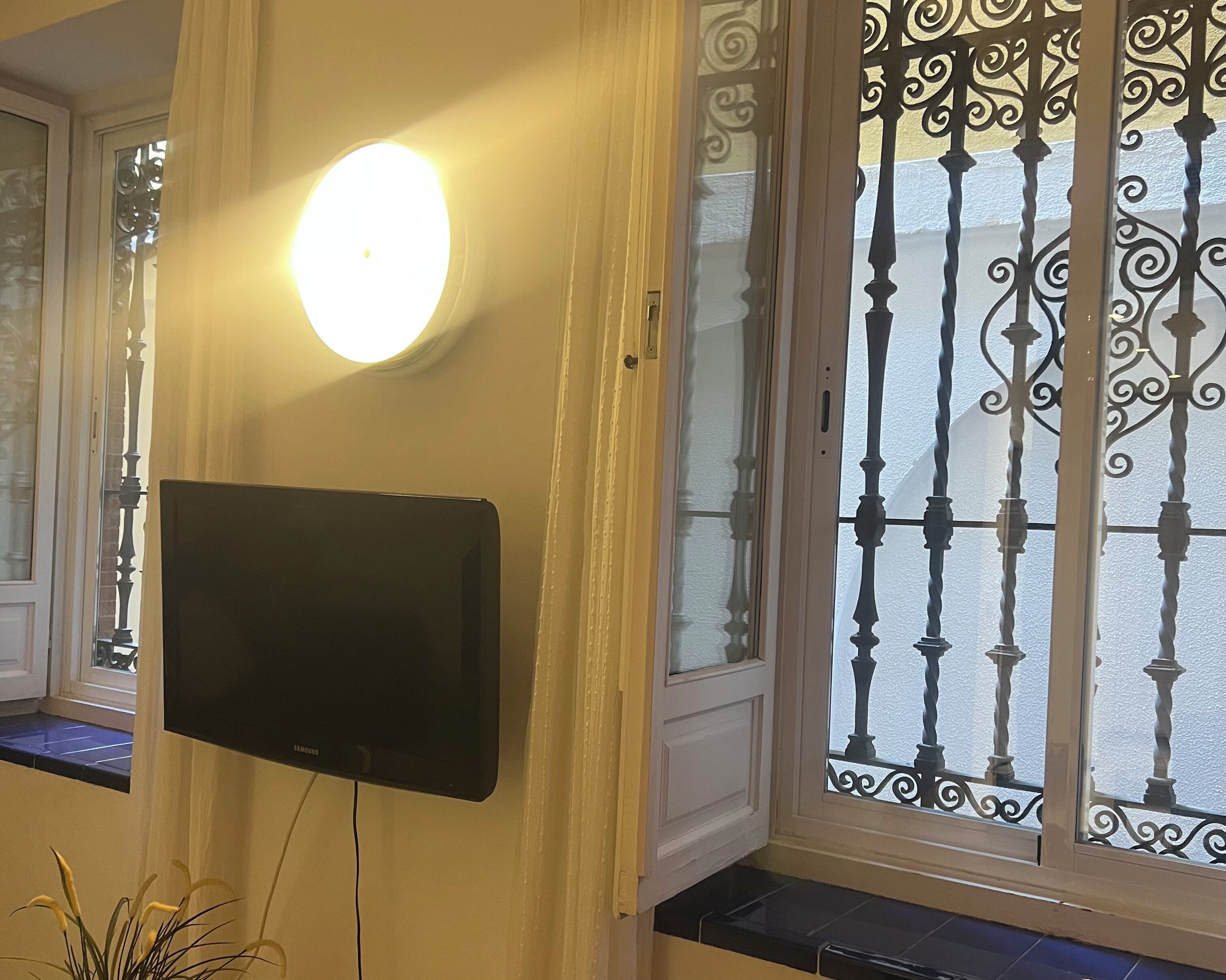 A room with a mounted flat-screen TV, a round wall light, and a decorative iron gate.