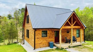 Une cabane en rondins avec un toit en métal, une véranda avec deux chaises et une petite fenêtre.