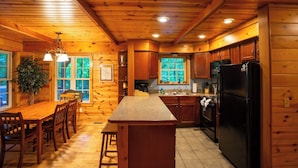 A wooden cabin interior with a kitchen, dining area, and a large window. - Blues Moon RRG - Hot tub | Wifi | Foosball Table! (Stanton)
