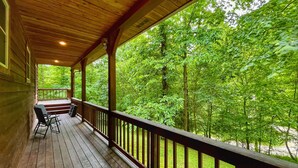 A wooden deck with a railing, a table, and two chairs, overlooking a dense forest. - Blues Moon RRG - Hot tub | Wifi | Foosball Table! (Stanton)