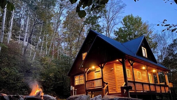 A log cabin with a fire pit in front, surrounded by rocks and trees. - Blues Moon RRG - Hot tub | Wifi | Foosball Table! (Stanton)