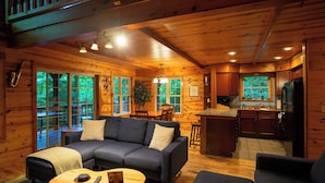 A log cabin interior with a sofa, coffee table, and kitchen area. - Blues Moon RRG - Hot tub | Wifi | Foosball Table! (Stanton)