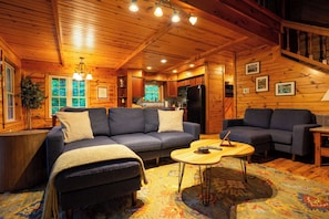 A cozy log cabin interior with a sofa, a coffee table, and a staircase.