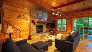 A log cabin interior with a stone fireplace, wooden walls, a sofa, and a television. - Blues Moon RRG - Hot tub | Wifi | Foosball Table! (Stanton)