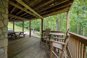 Une terrasse en bois, agrémentée de tables et de chaises pour pique-niquer, entourée d’arbres.