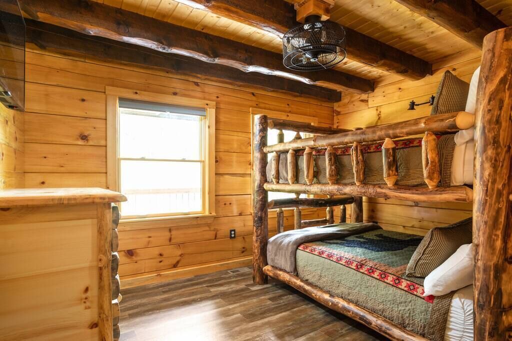 A rustic wooden cabin interior with a bunk bed, a window, and a ceiling fan.