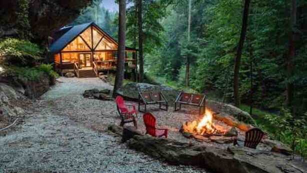 A cabin with a stone fire pit and red chairs, surrounded by a forest. - Cabin of Freedom Falls -Private Waterfall, Hot Tub- Secluded & Luxury Log Cabin Retreat (Slade)