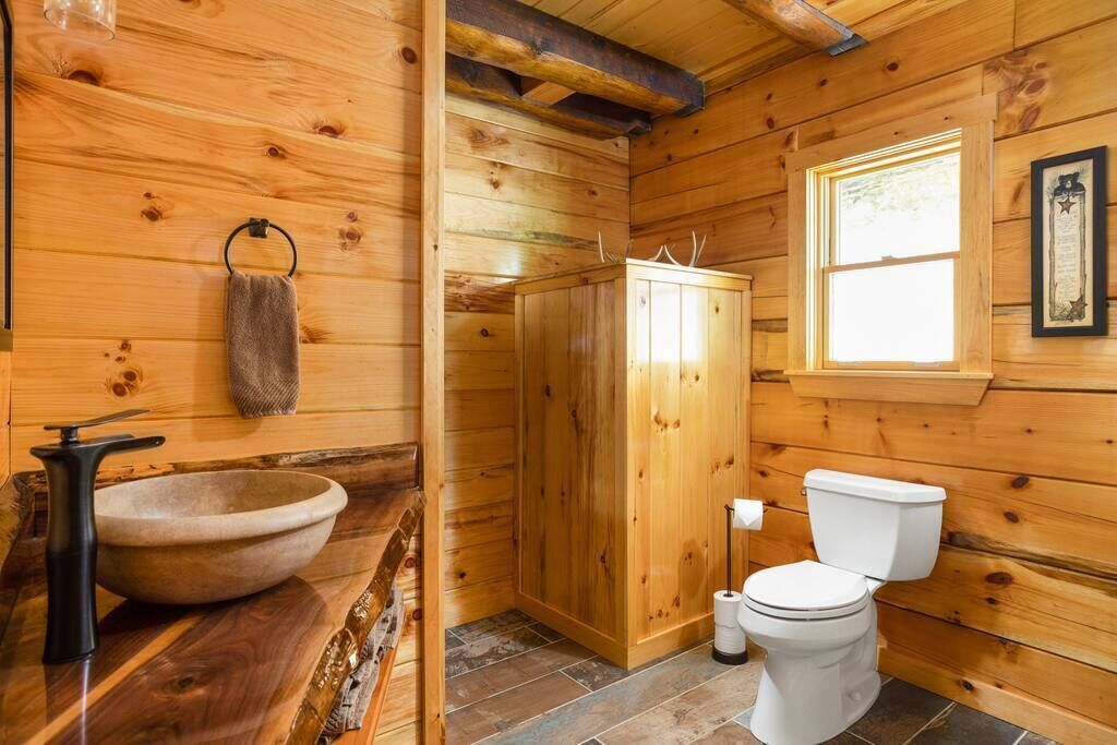 A wooden cabin bathroom with a stone sink, a toilet, and a shower area.