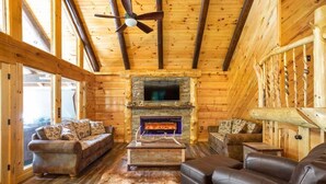 A log cabin interior with a fireplace, leather sofas, and a ceiling fan. - Cabin of Freedom Falls -Private Waterfall, Hot Tub- Secluded & Luxury Log Cabin Retreat (Slade)