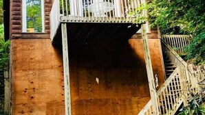 A wooden cabin with a balcony, surrounded by dense green foliage. - Cozy RRG Retreat | Private Valley & Forest Views | Hidden Falls Cabin (Campton)