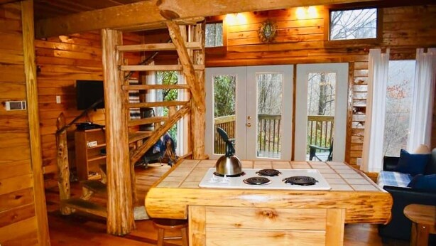 A wooden cabin interior with a kitchen area featuring a stove, a ladder, and a dining table. - Cozy RRG Retreat | Private Valley & Forest Views | Hidden Falls Cabin (Campton)