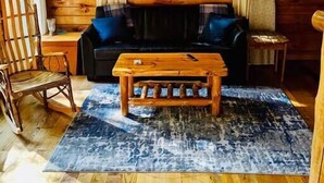 A cozy room with a wooden floor, a sofa, a coffee table, and a window with curtains. - Cozy RRG Retreat | Private Valley & Forest Views | Hidden Falls Cabin (Campton)