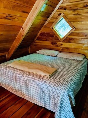 Una stanza in legno con soffitto spiovente, una piccola finestra, un letto con copriletto decorato e un cuscino.