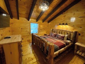 Une chambre dans une cabane en bois, avec un lit, un petit bureau et une fenêtre.