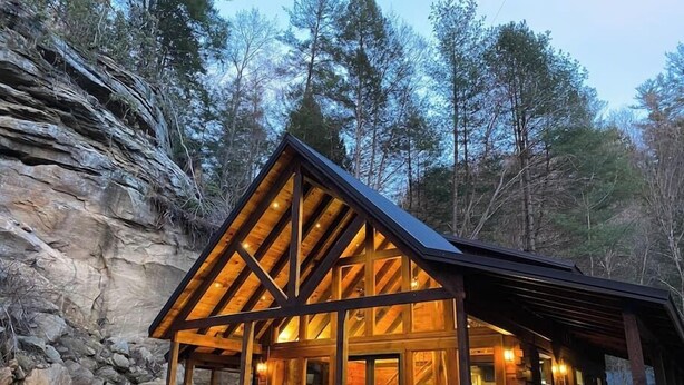 Eine Holzhütte mit geneigtem Dach, großen Fenstern und einer Treppe zum Eingang.