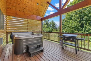 A wooden deck with a hot tub, grill, and outdoor seating area.