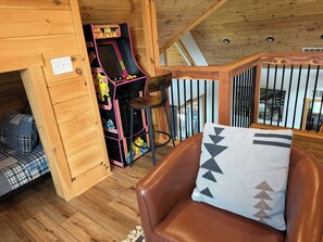 A cozy room with a brown leather chair, a small table, and a colorful arcade machine.