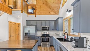 A modern kitchen with grey cabinets, stainless steel appliances, a wooden dining table, and a wooden staircase.