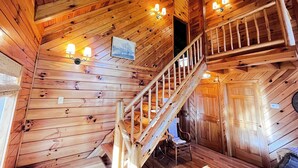 A wooden cabin interior with a wooden staircase, a ceiling fan, and wall-mounted lights. - Horseshoe Falls-RRG-Hot tub! (Rogers)