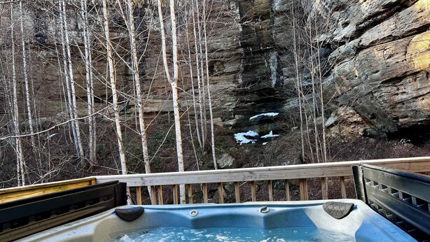 A hot tub with a wooden deck, surrounded by rocky cliffs and bare trees. - Horseshoe Falls-RRG-Hot tub! (Rogers)