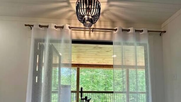 Um banheiro moderno com uma banheira independente, um lustre no teto e vista para uma varanda com árvores.