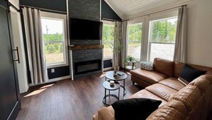 Uma sala de estar moderna com lareira, janelas amplas, um sofá de couro e uma pequena mesa.