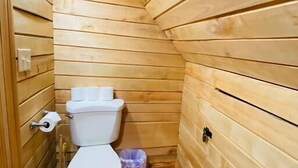 A small, wooden-paneled bathroom with a toilet, a trash bin, and a vent on the ceiling. - Mountain Chalet |Hot Tub | Centrally Located | RRG (Campton)