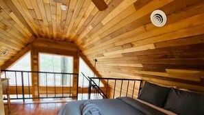A bedroom with a sloped ceiling, wooden flooring, a bed with a blue mattress, and a ceiling fan. - Mountain Chalet |Hot Tub | Centrally Located | RRG (Campton)