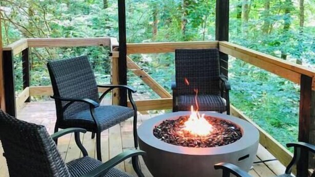Un patio in legno con un focolare e poltrone in vimini, immerso in una zona boscosa.