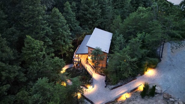 A cabin surrounded by dense forest, with a gravel path leading to the entrance.